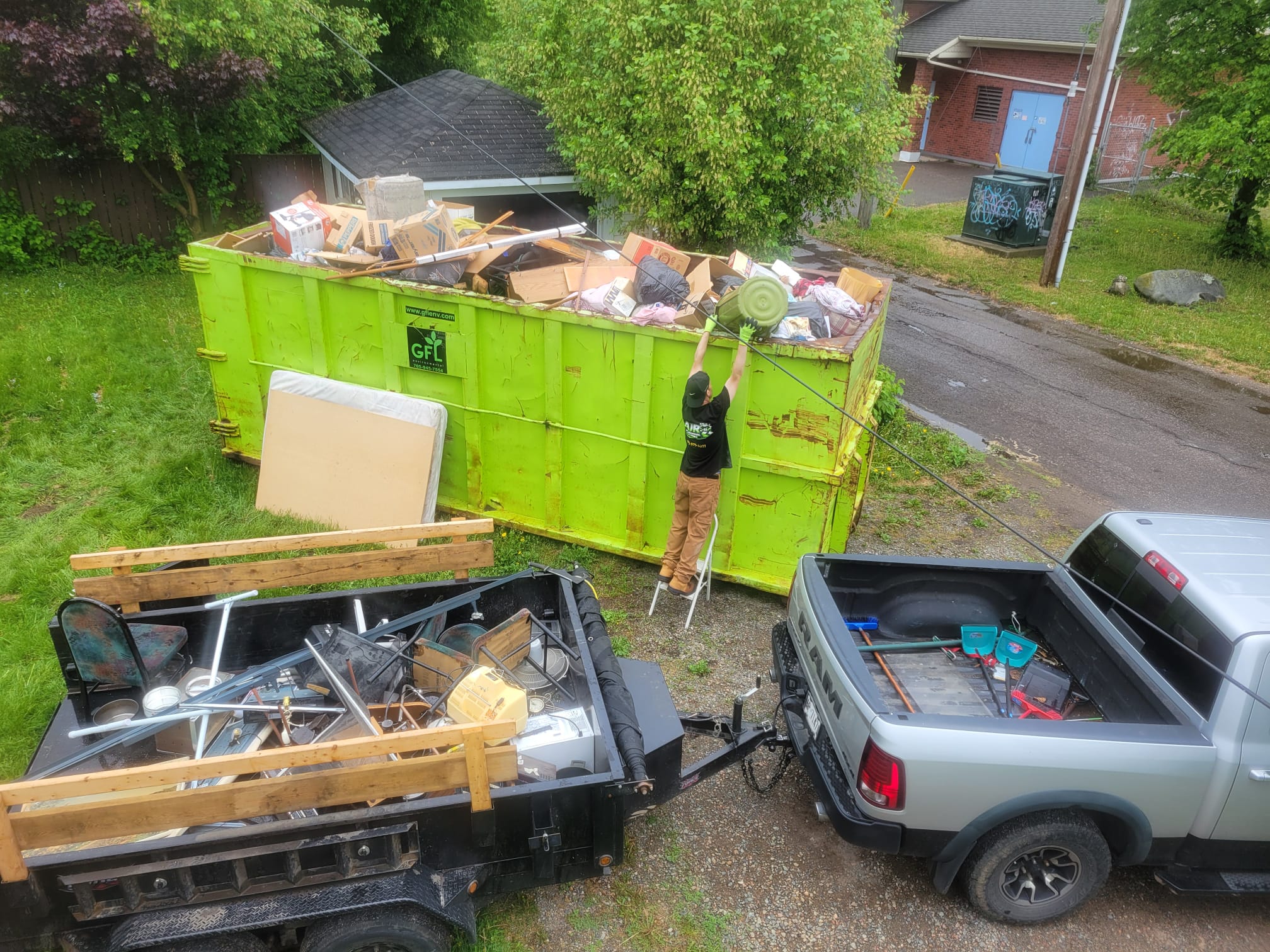A large dumpster filled with debris next to a residential driveway.